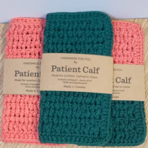 A set of three hand-crocheted washcloths in Tangerine and Forest Green with Patient Calf paper branding wraps.