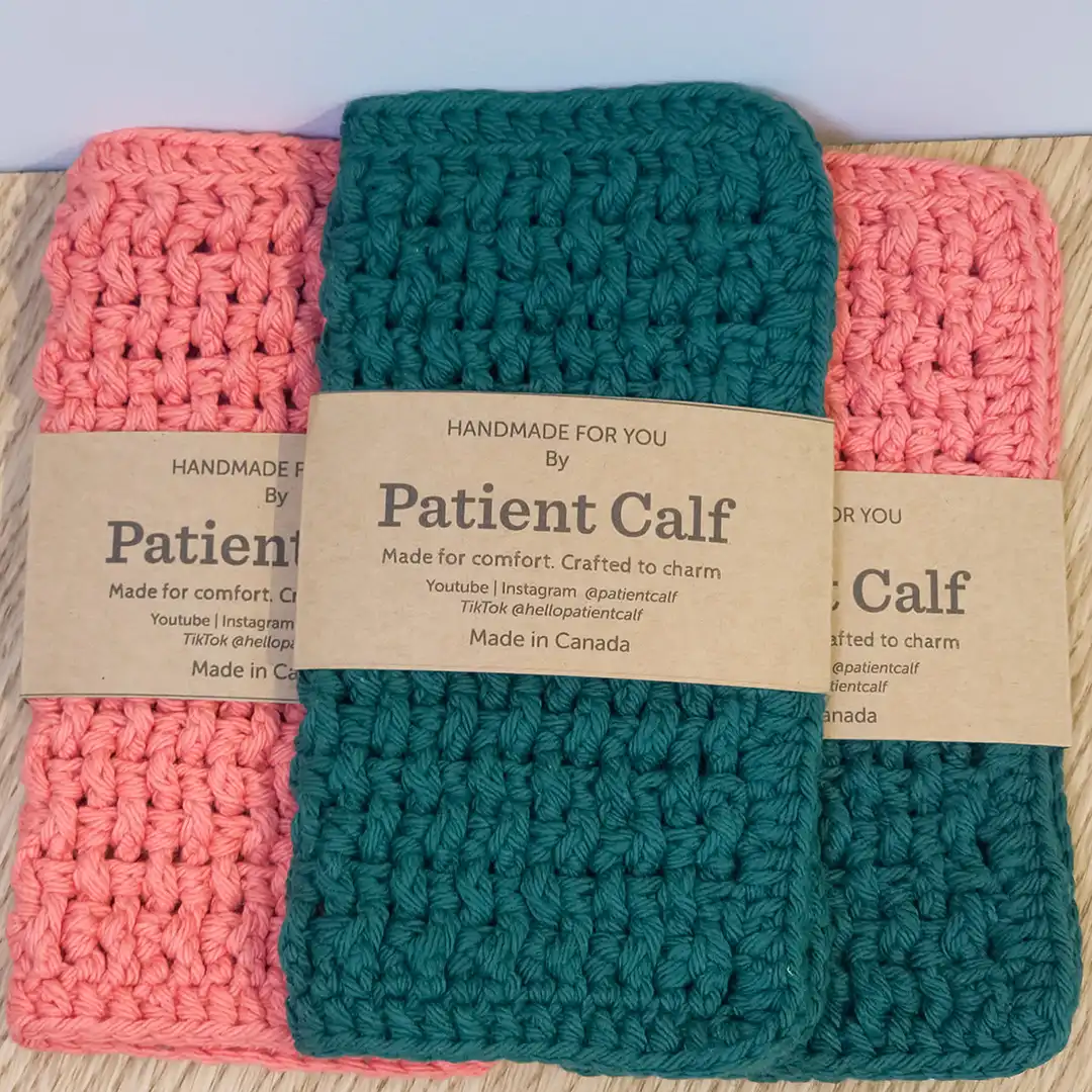 A set of three hand-crocheted washcloths in Tangerine and Forest Green with Patient Calf paper branding wraps.
