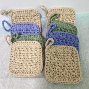 Two stacks of 4 handmade cotton face scrubbies by Patient Calf, showing the thick, textured crochet stitch and hanging loops in assorted earthy tones.