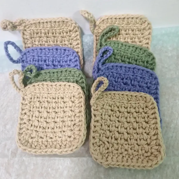Two stacks of 4 handmade cotton face scrubbies by Patient Calf, showing the thick, textured crochet stitch and hanging loops in assorted earthy tones.