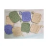 An assorted set of 8 square crochet face scrubbies in earthy sand, sage green, and lilac colors spread out to show texture and hanging loops.