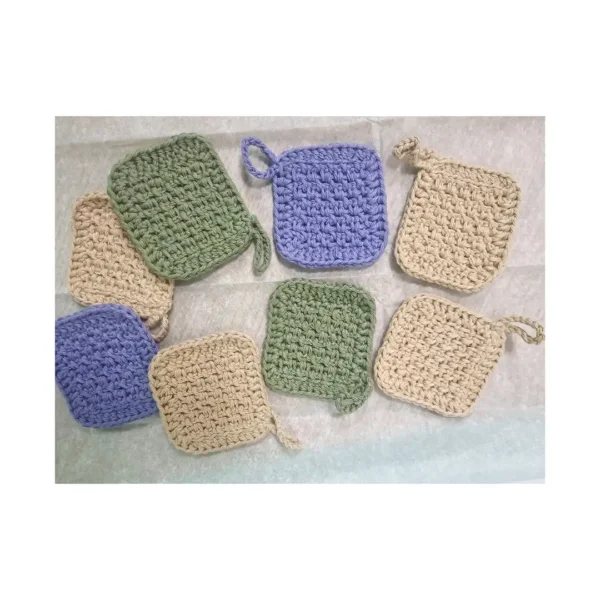 An assorted set of 8 square crochet face scrubbies in earthy sand, sage green, and lilac colors spread out to show texture and hanging loops.