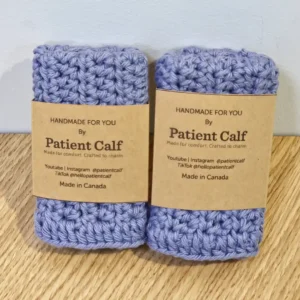 A stacked set of two handmade periwinkle blue cotton washcloths by Patient Calf, featuring brown paper branding bands and "Made in Canada" labels.