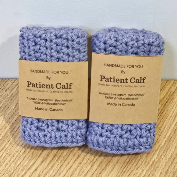 A stacked set of two handmade periwinkle blue cotton washcloths by Patient Calf, featuring brown paper branding bands and "Made in Canada" labels.