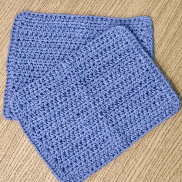 Two overlapping handmade periwinkle cotton washcloths showing the soft, breathable crochet texture and handmade quality.