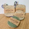 A mixed set of 6 handmade cotton face scrubbies by Patient Calf, featuring 4 square scrubbies with hanging loops and 2 round crochet discs in earthy sand, sage green, and periwinkle-lilac tones.