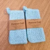 Two hand-crocheted light blue cotton washcloths with hanging loops by Patient Calf, featuring a textured stitch for skincare exfoliation.