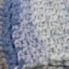 A close-up view of the textured crochet stitch and soft blue and grey stripes of the Drina Scarf.
