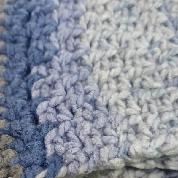 A close-up view of the textured crochet stitch and soft blue and grey stripes of the Drina Scarf.
