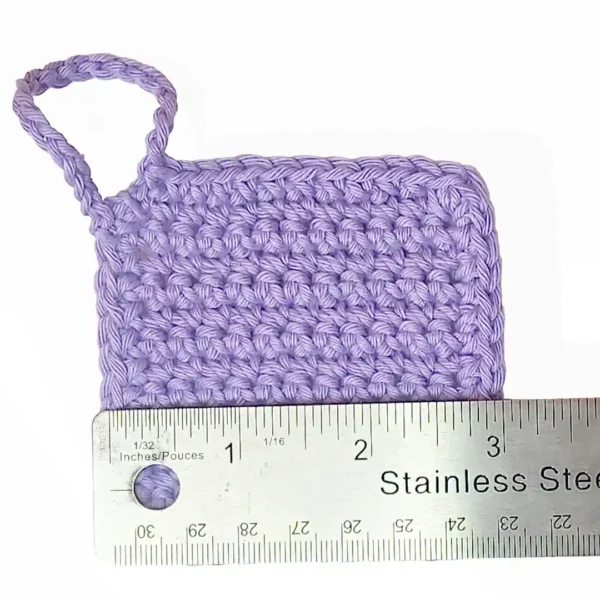 Close-up of a soft lilac Iris scrubbie by Patient Calf measured with a stainless steel ruler to show the 3 inch (7.6 cm) width.